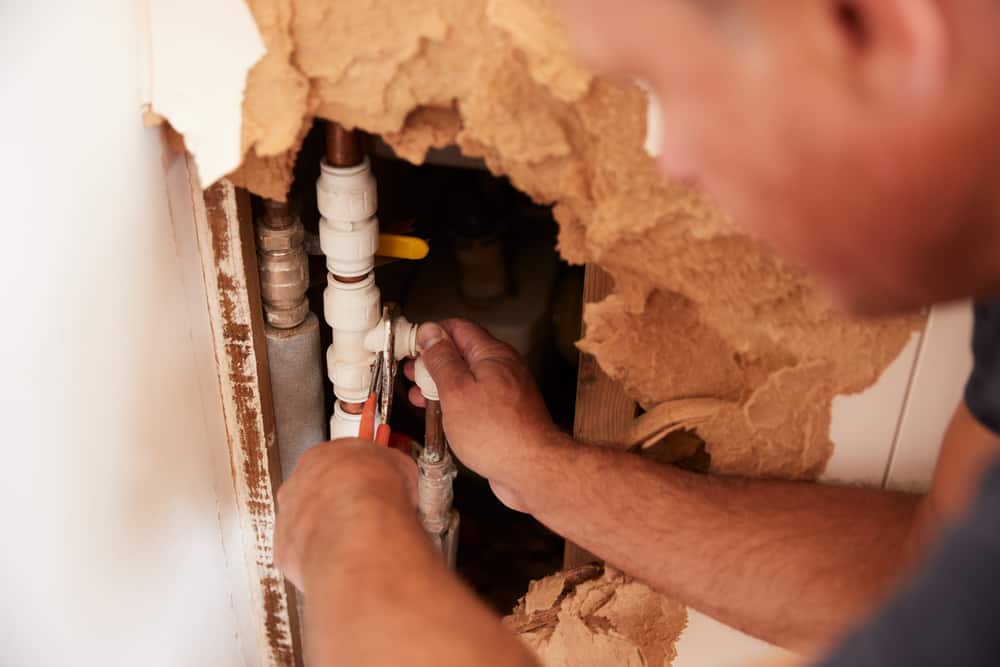 plumber repairing a broken pipe in a wall.