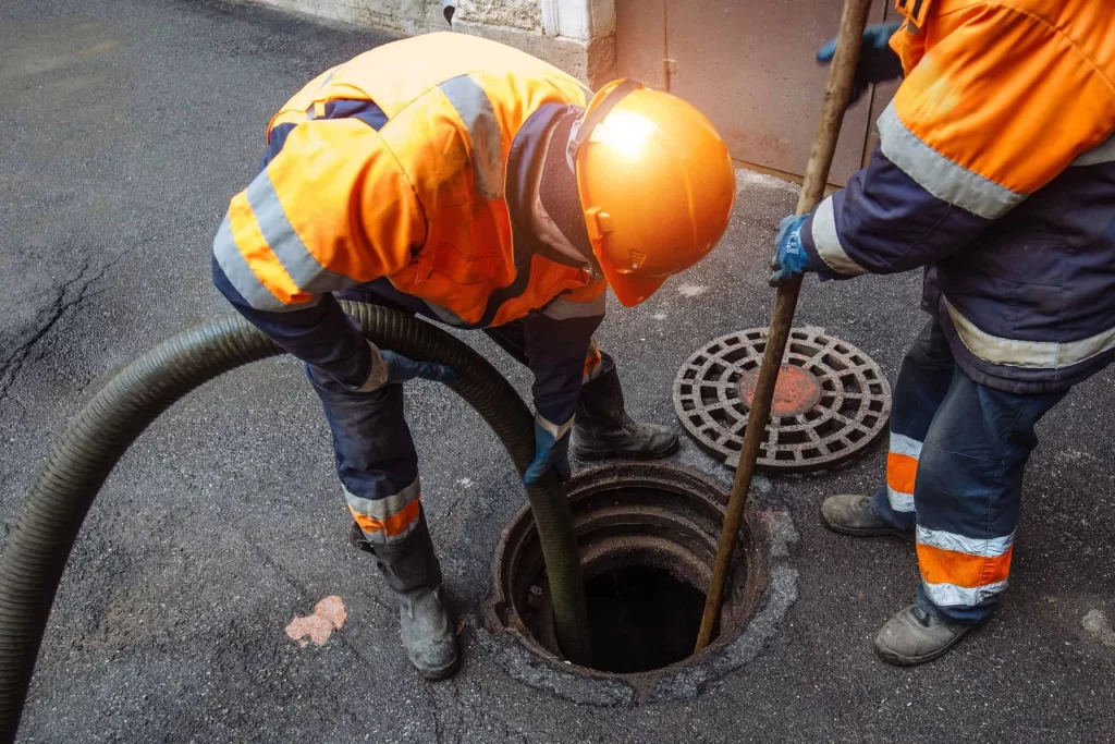 A sewer maintenance workers cleaning a manhole and clearing blockages from sewers near a sidewalk