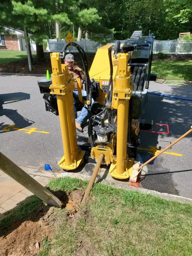 Worker drilling a hole in the ground using yellow trenchless plumbing equipment on a job site in Long Island, NY. The worker is focused on the task, with the trenchless technology machinery visible, showcasing the efficient and non-invasive method used for sewer and water line installation