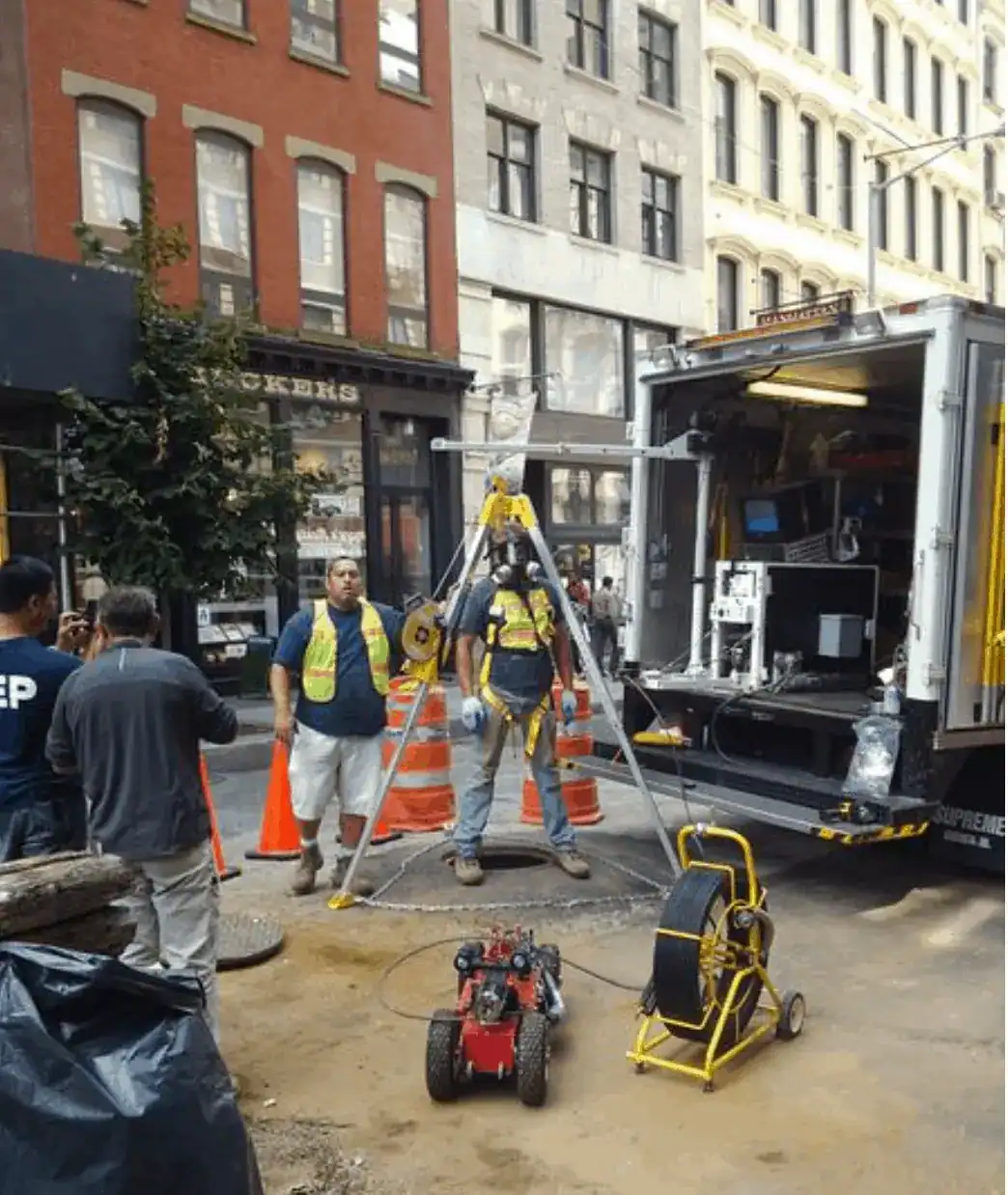 Street construction workers operating heavy machinery and equipment on a busy road in Nassau County, NY, with safety cones, barriers, and high-visibility vests visible under a clear daytime sky.