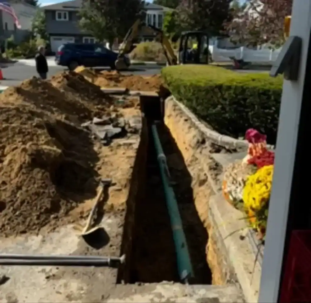 Construction workers performing trench excavation and pipe installation at a residential site in Nassau County, NY, with heavy machinery and safety equipment visible.