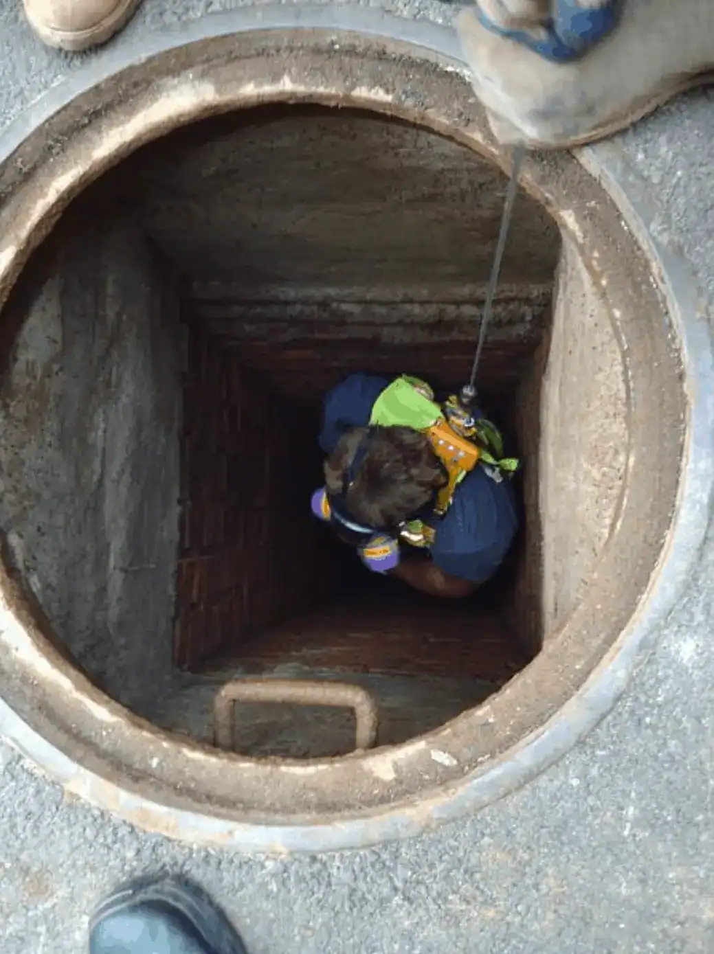 A worker wearing safety gear, including a hard hat and reflective vest, is carefully entering a manhole in Nassau County, New York, preparing for underground maintenance or inspection work.